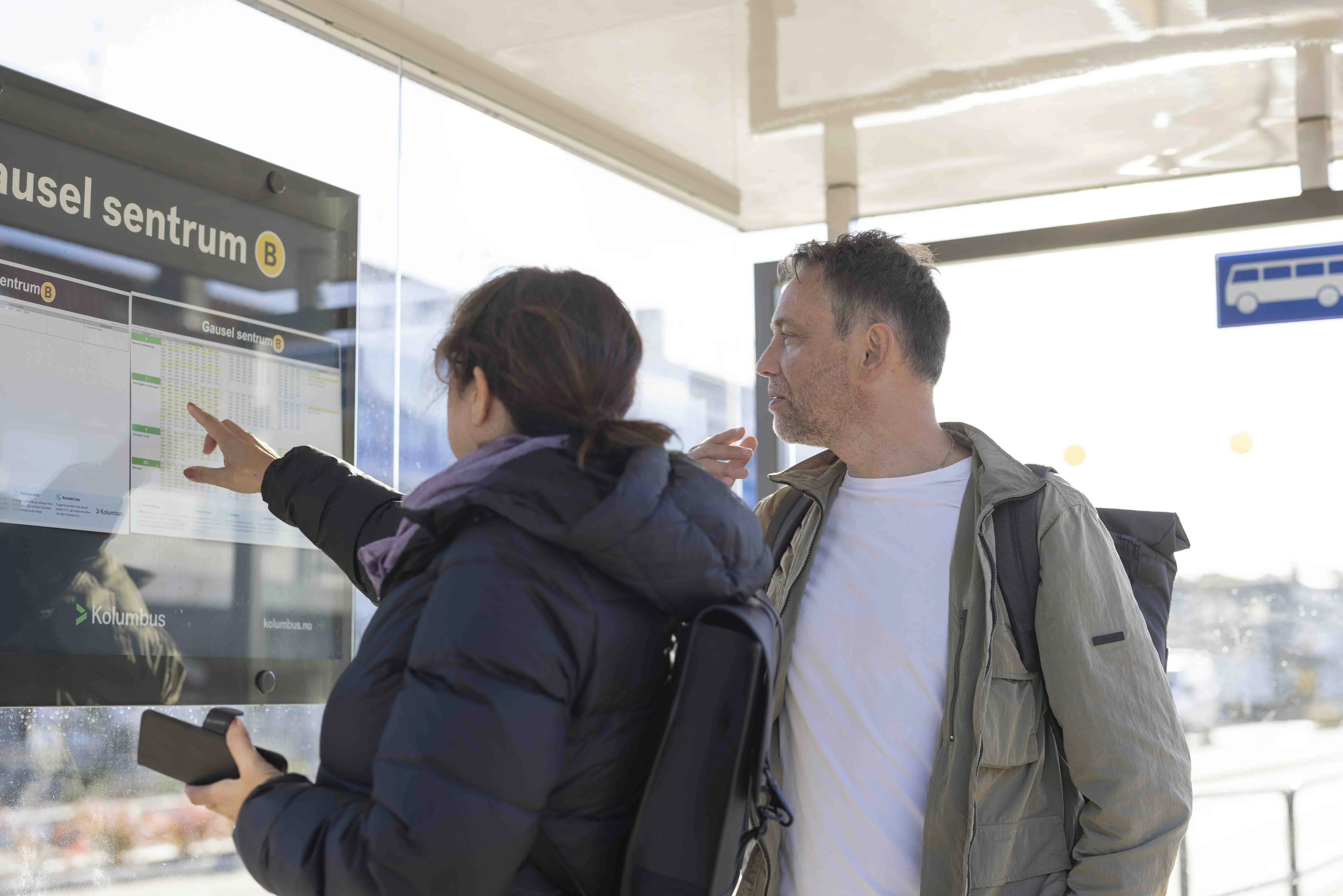 To personer ser på rutetavlen på holdeplassen Gausel sentrum
